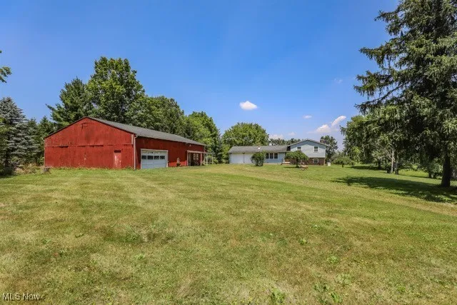 View of grassy yard with a detached garage, an outdoor structure, and an outbuilding