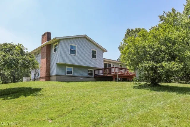 Back of house featuring a chimney, a lawn, and a wooden deck