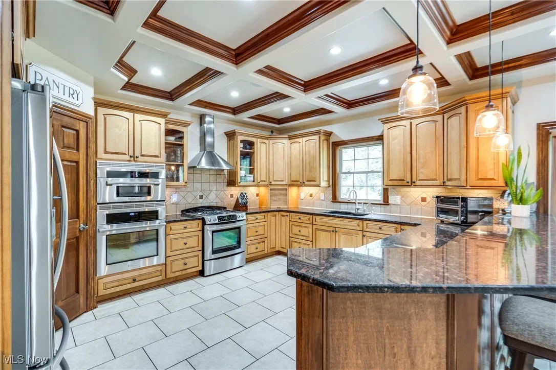 Kitchen with appliances with stainless steel finishes, wall chimney exhaust hood, a peninsula, a breakfast bar, and tasteful backsplash