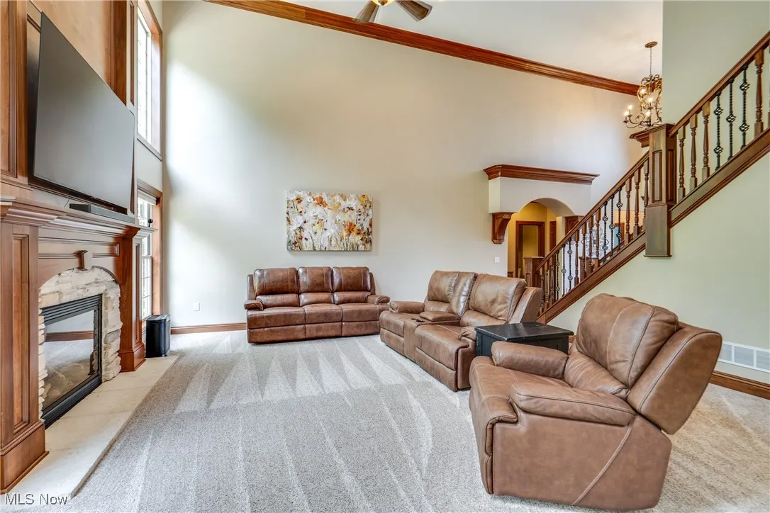 Carpeted living area with a fireplace, ornamental molding, a towering ceiling, stairs, and arched walkways