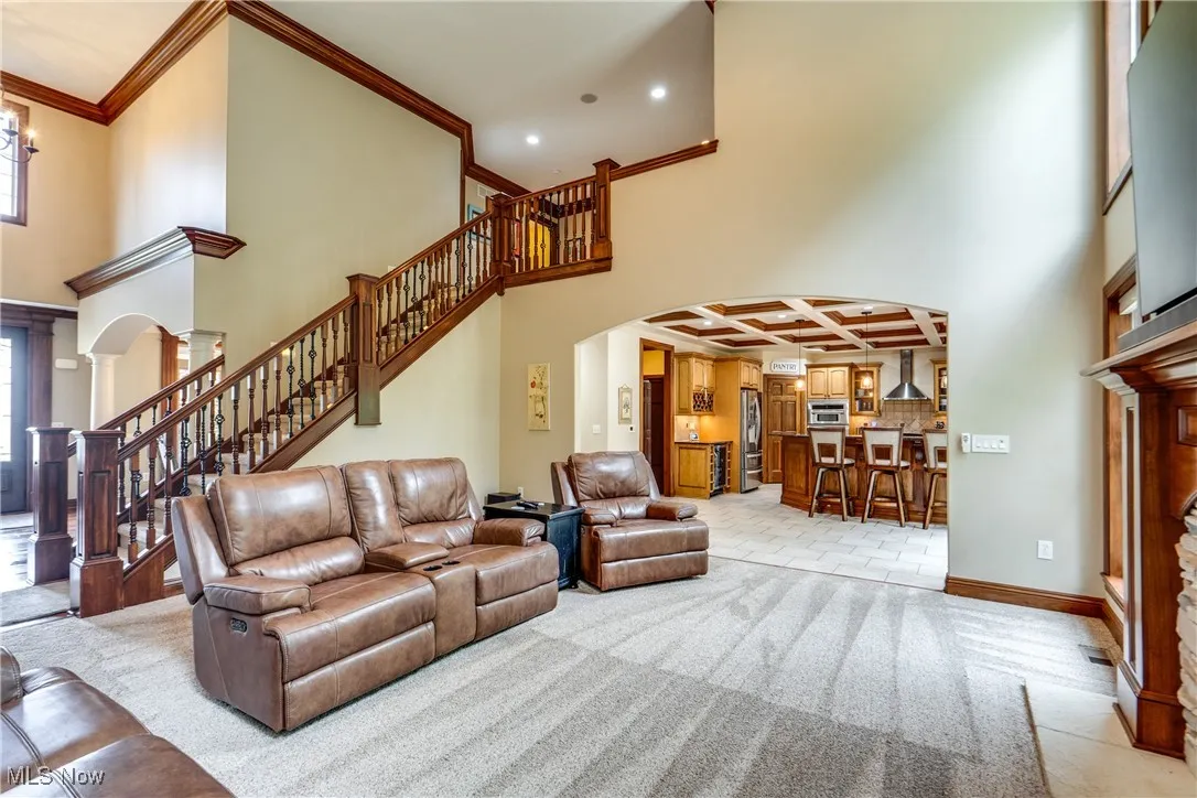 Living room with arched walkways, crown molding, coffered ceiling, a high ceiling, and stairs