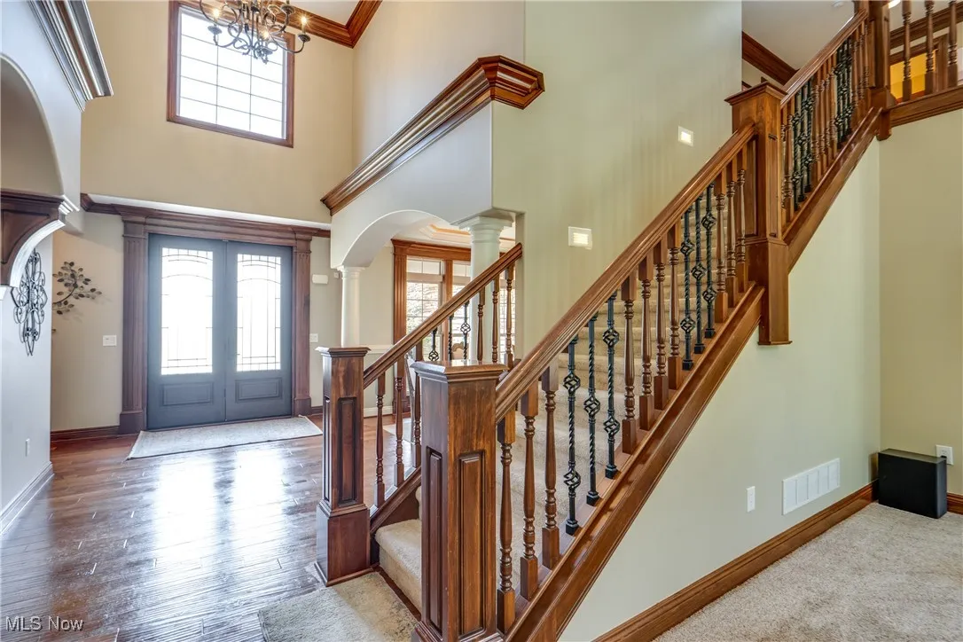 Entryway with a towering ceiling, a chandelier, stairs, arched walkways, and crown molding