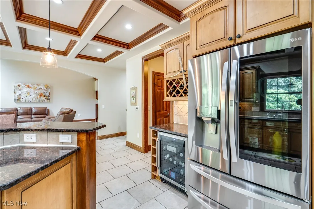 Kitchen with stainless steel refrigerator with ice dispenser, beverage cooler, tasteful backsplash, light tile patterned floors, and dark stone counters