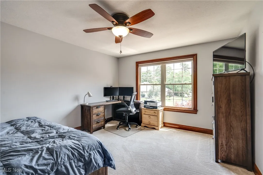 Bedroom with light colored carpet, a ceiling fan, and a desk