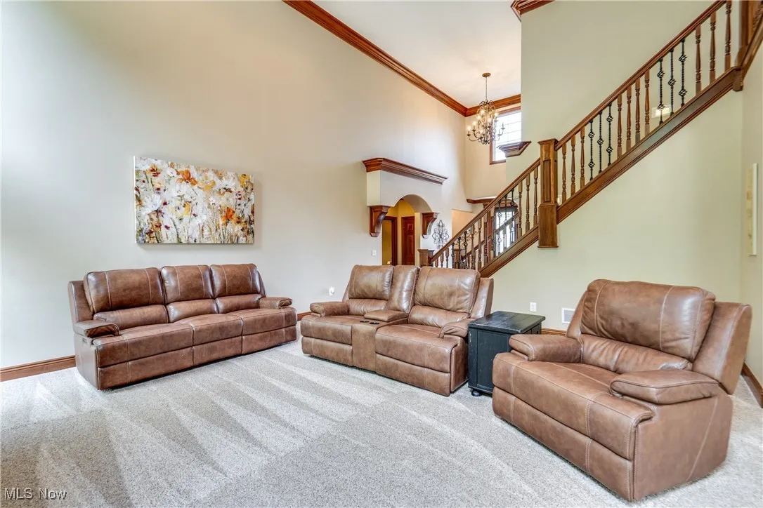 Living area featuring carpet floors, a chandelier, a high ceiling, stairs, and crown molding