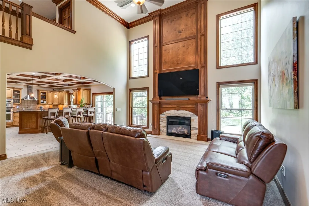 Living room with arched walkways, light colored carpet, plenty of natural light, ceiling fan, and a towering ceiling