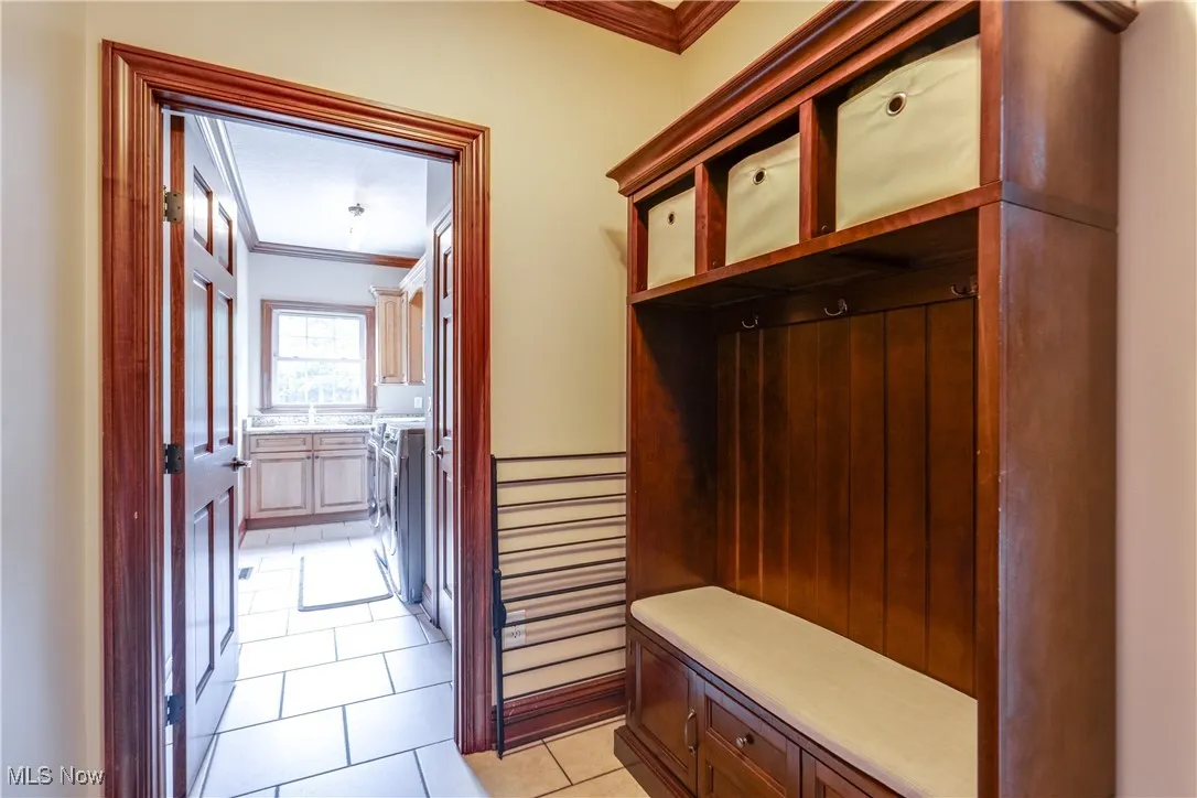 Mudroom with crown molding, washing machine and clothes dryer, and light tile patterned flooring