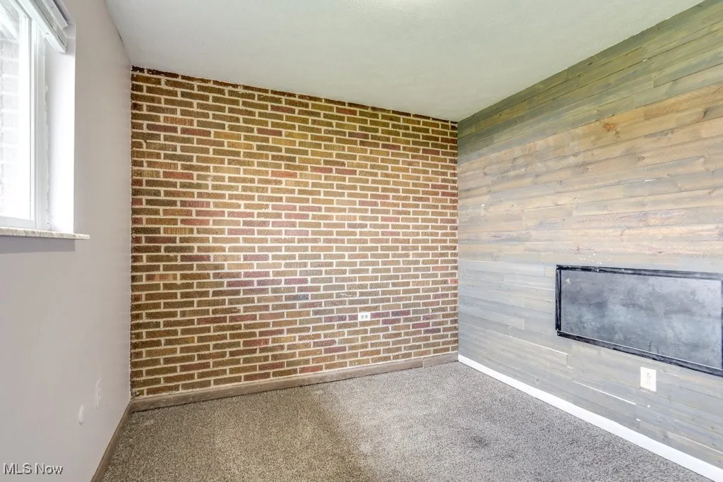 Carpeted empty room with wood walls, baseboards, and a glass covered fireplace