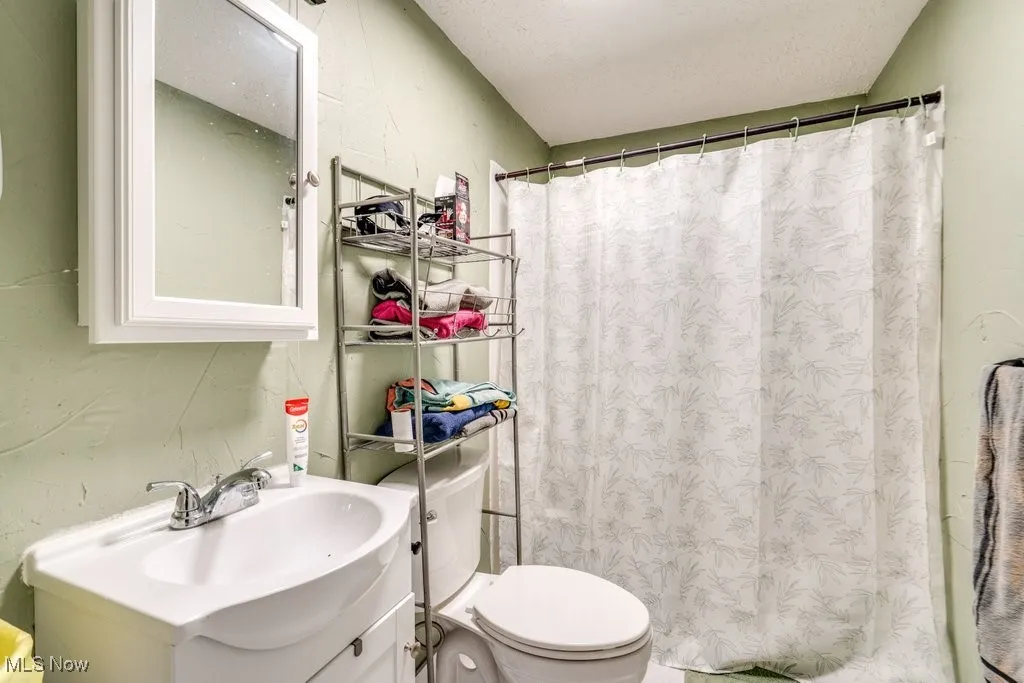 Full bath featuring curtained shower, vanity, a textured ceiling, and toilet