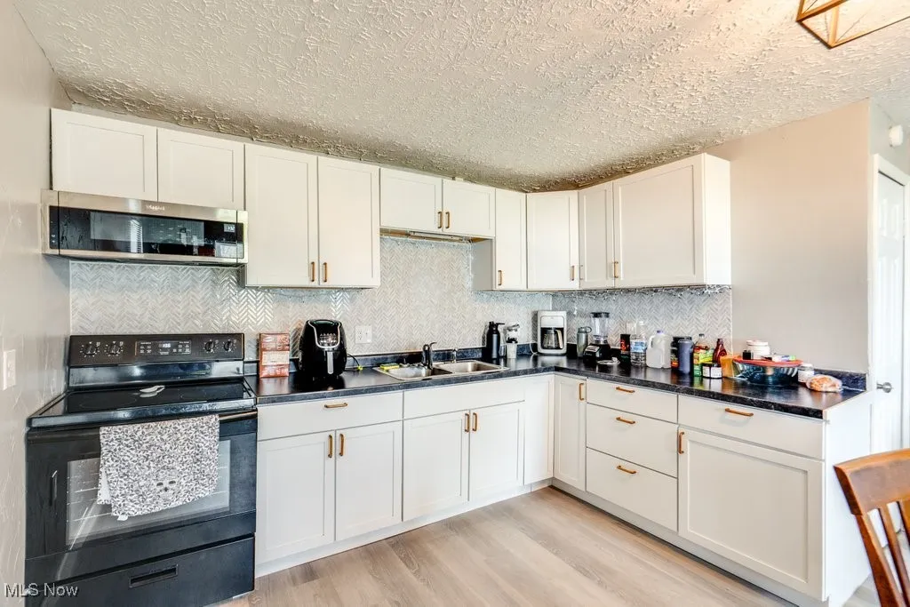 Kitchen featuring stainless steel microwave, white cabinetry, light wood-style floors, black range with electric cooktop, and a sink