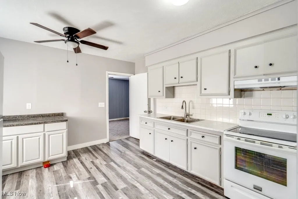 Kitchen featuring ceiling fan, electric range, under cabinet range hood, a sink, and backsplash