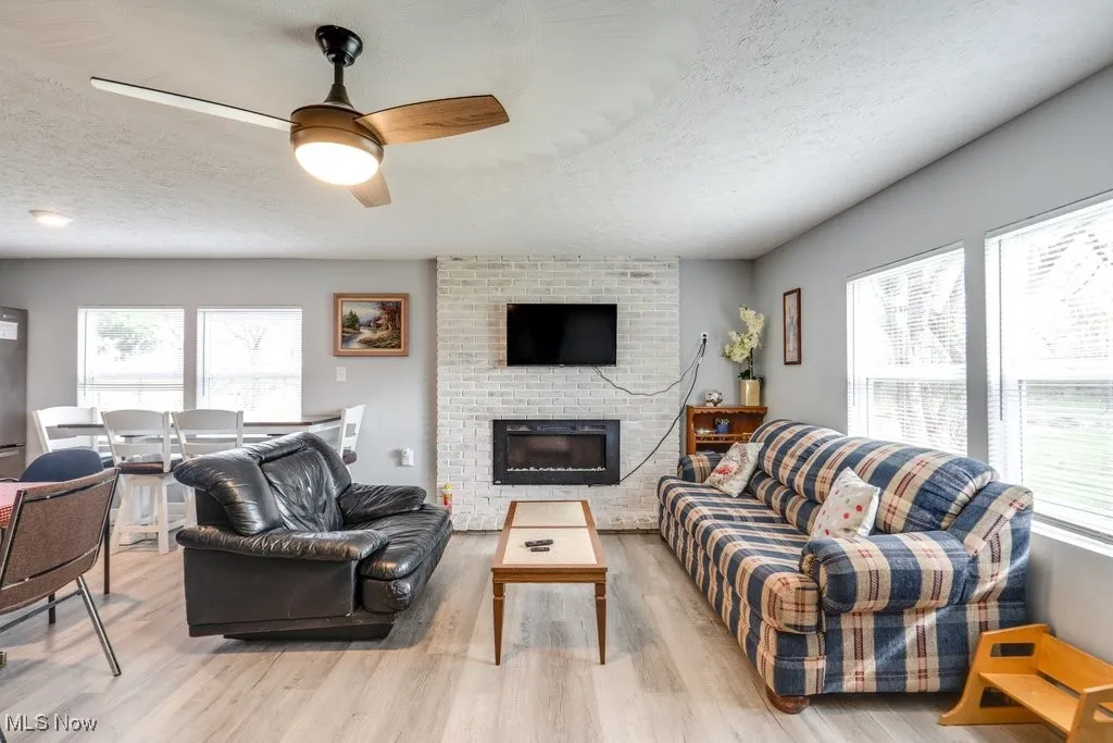 Living area with light wood-style flooring, a ceiling fan, and a textured ceiling