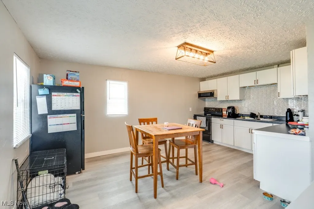 Kitchen with electric stove, white cabinetry, backsplash, and light wood finished floors