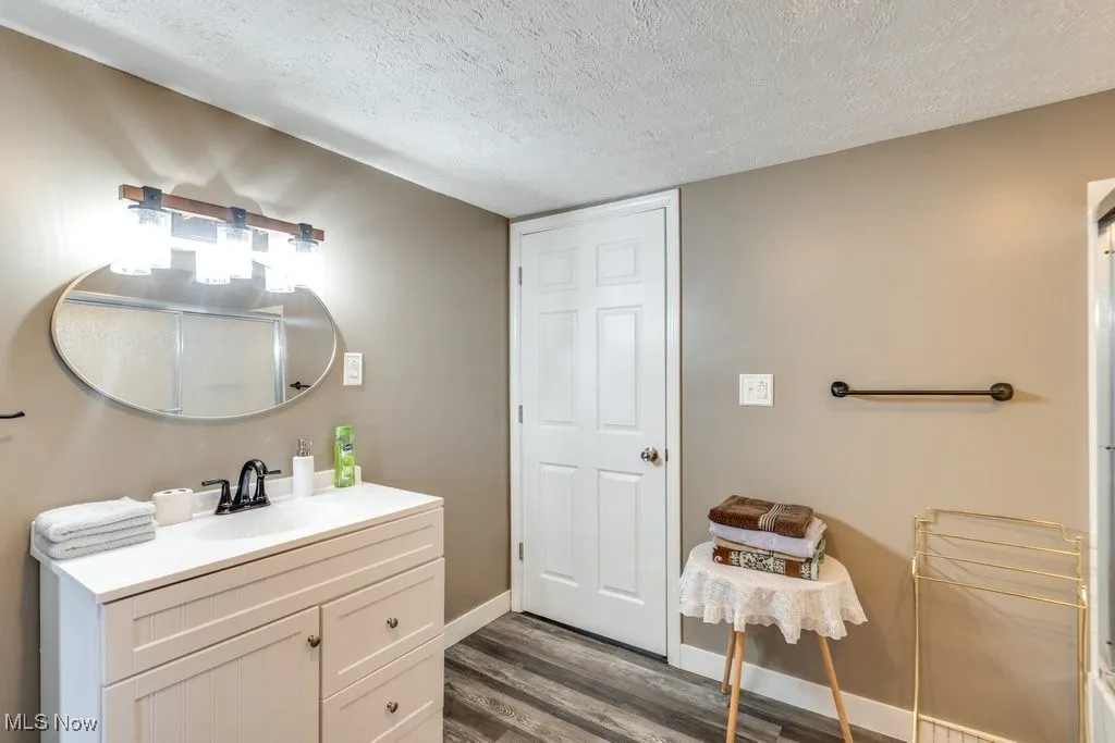 Bathroom with vanity, a textured ceiling, baseboards, and wood finished floors