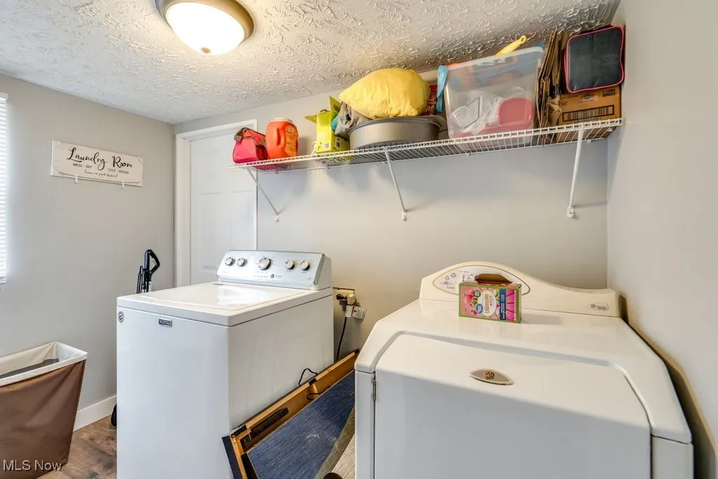 Clothes washing area with baseboards, washing machine and dryer, a textured ceiling, laundry area, and wood finished floors