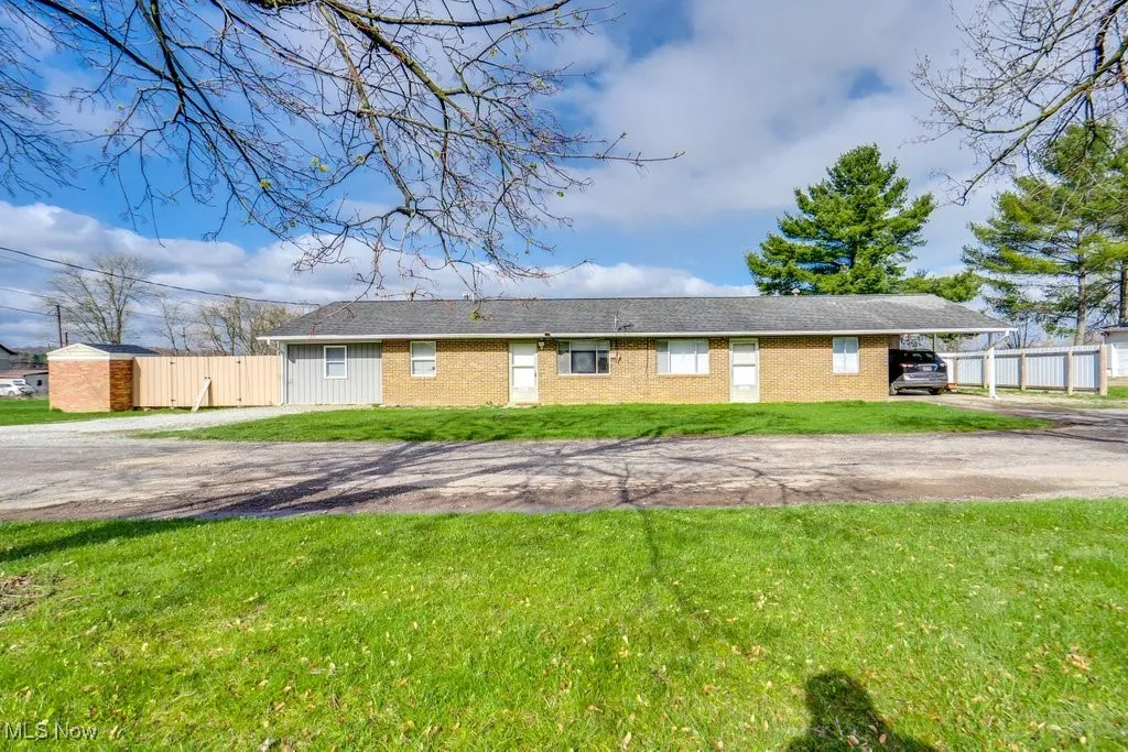 Rear view of house featuring dirt driveway, brick siding, fence, and a lawn