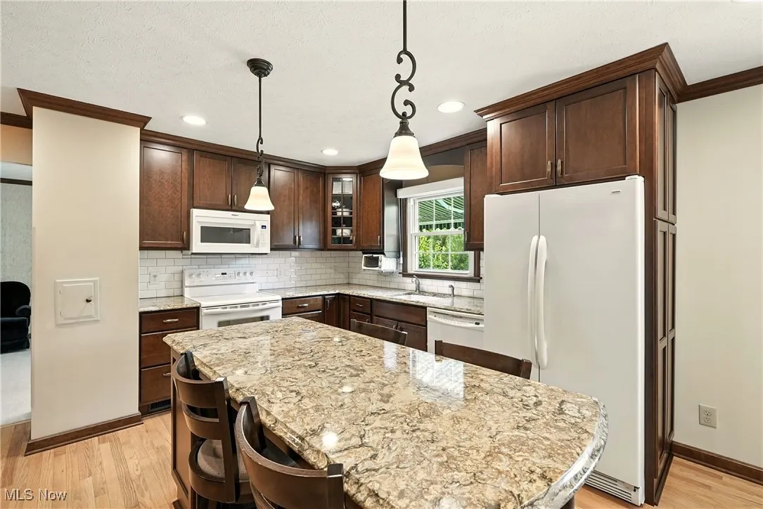 Kitchen with white appliances, crown molding, light wood-style flooring, dark brown cabinetry, and decorative backsplash