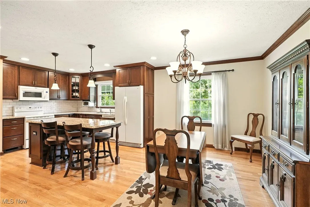 Dining space featuring healthy amount of natural light, a textured ceiling, ornamental molding, a chandelier, and light wood-style floors