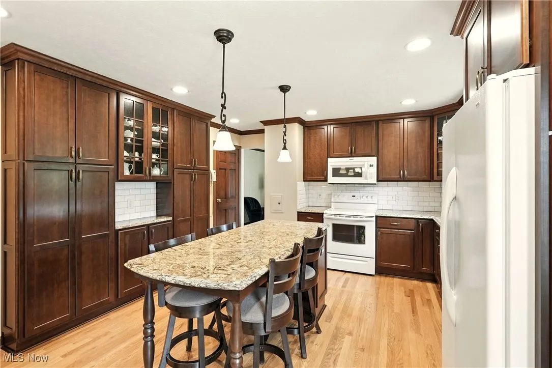 Kitchen with white appliances, decorative backsplash, light wood finished floors, light stone counters, and recessed lighting
