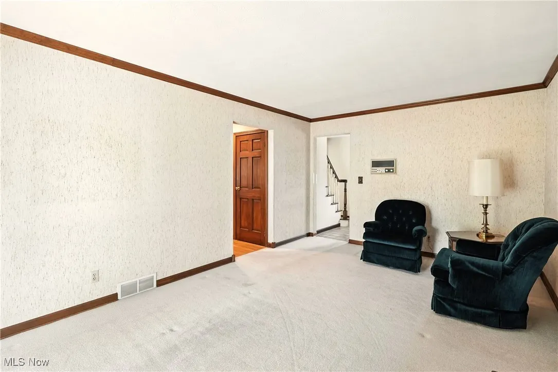 Sitting room with stairs, ornamental molding, and carpet flooring