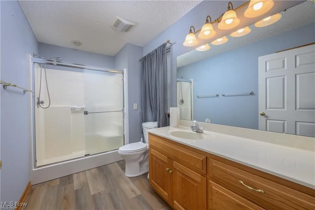Full bathroom with wood finished floors, a shower stall, vanity, and a textured ceiling