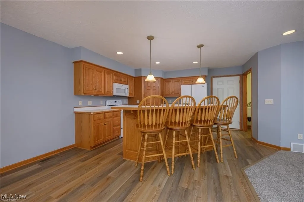 Kitchen with white appliances, wood finished floors, light countertops, pendant lighting, and a kitchen island