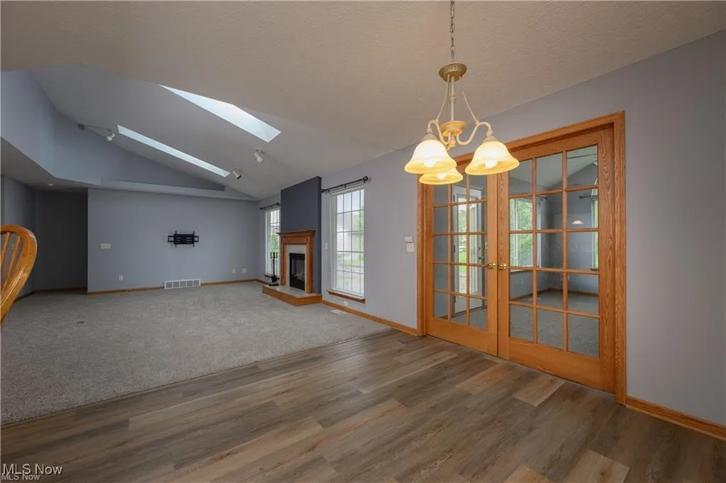 Unfurnished living room featuring wood finished floors, vaulted ceiling, a skylight, a chandelier, and a glass covered fireplace