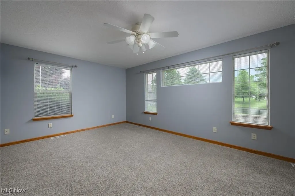 Carpeted empty room featuring healthy amount of natural light, a ceiling fan, and a textured ceiling