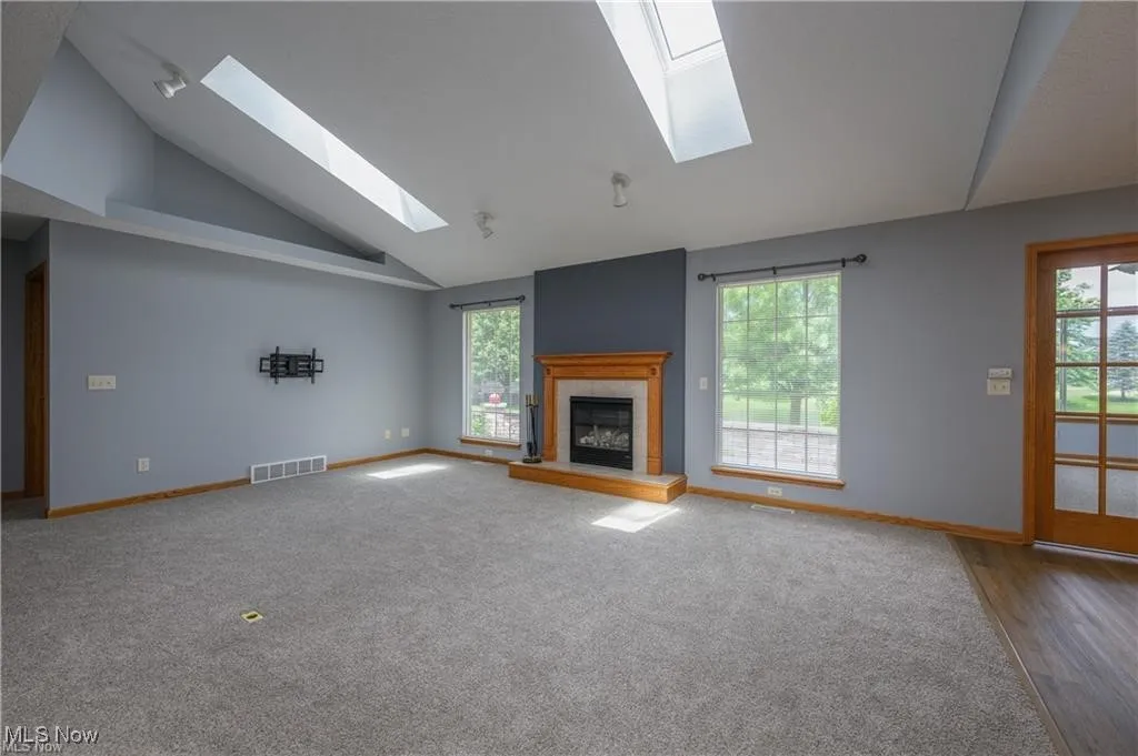 Unfurnished living room with a skylight, vaulted ceiling, a fireplace, carpet floors, and wood finished floors