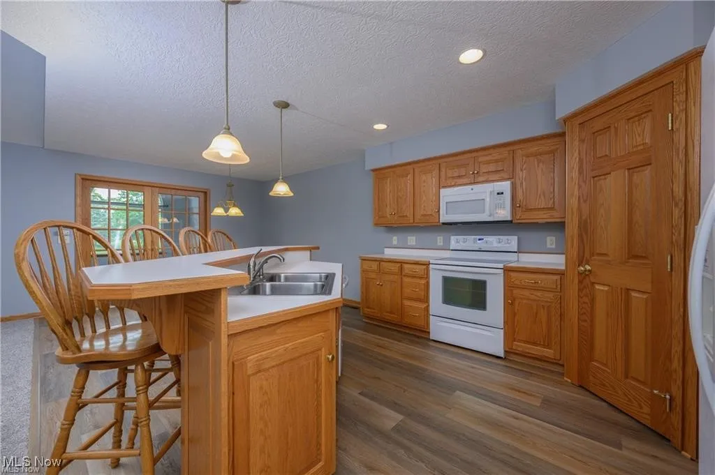 Kitchen with white appliances, a textured ceiling, a kitchen bar, light countertops, and an island with sink