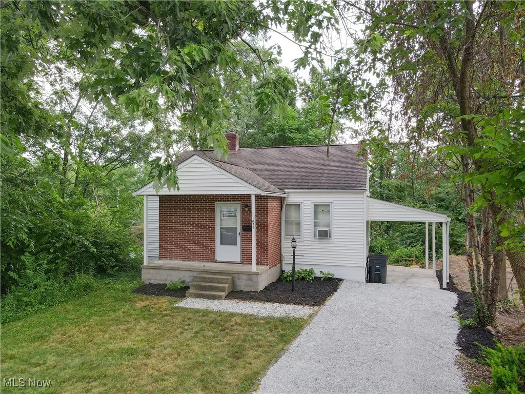 Bungalow-style home featuring a chimney, an attached carport, a front lawn, driveway, and brick siding