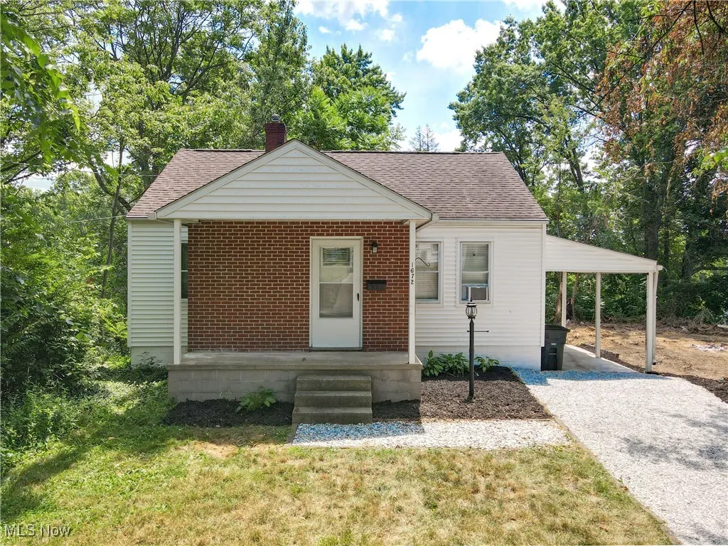 Bungalow-style home featuring a chimney, roof with shingles, a carport, gravel driveway, and a front lawn
