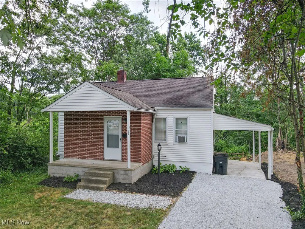 Bungalow with a chimney, brick siding, roof with shingles, and gravel driveway