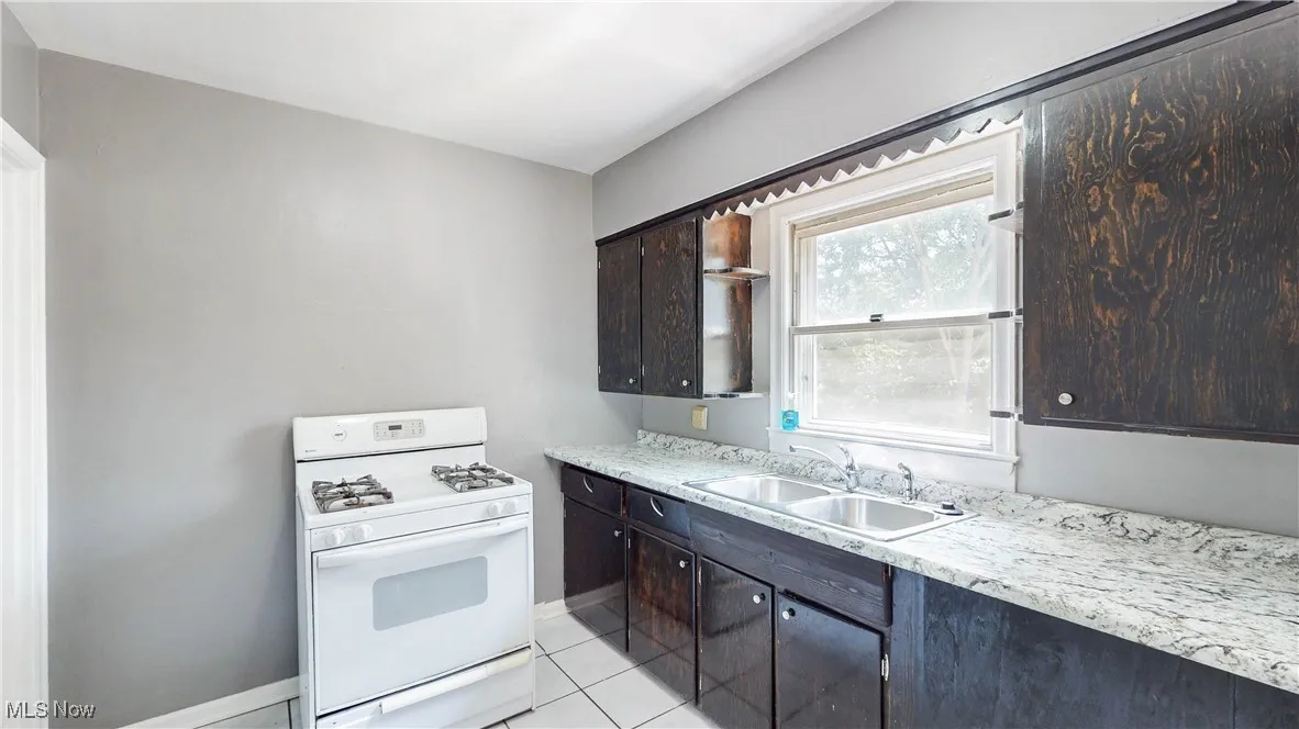 Kitchen with white gas range oven, dark brown cabinetry, and light tile patterned floors