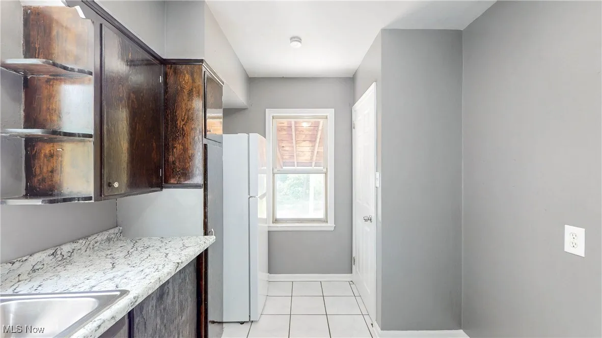Kitchen featuring dark brown cabinets, freestanding refrigerator, and light tile patterned floors