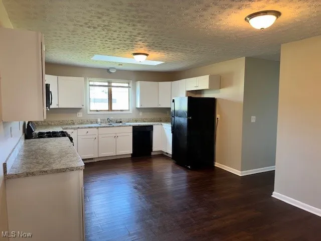 Kitchen with black appliances, dark wood-style floors, light countertops, and white cabinetry