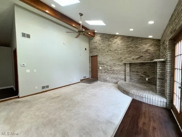 Unfurnished great room with a brick fireplace, high vaulted ceiling, ceiling fan, a skylight, and brick wall