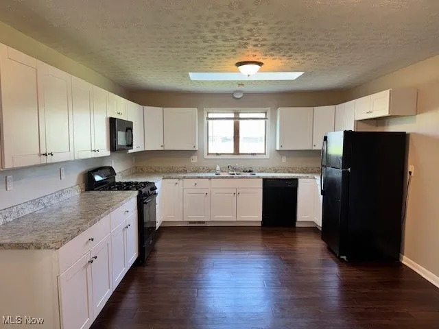 Kitchen featuring black appliances, white cabinetry, light countertops, dark wood-style floors, and a textured ceiling