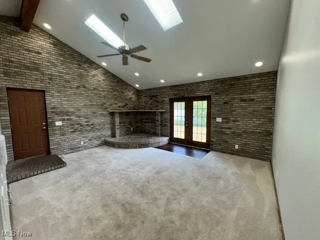 Unfurnished great room featuring a skylight, french doors, carpet floors, high vaulted ceiling, and brick wall