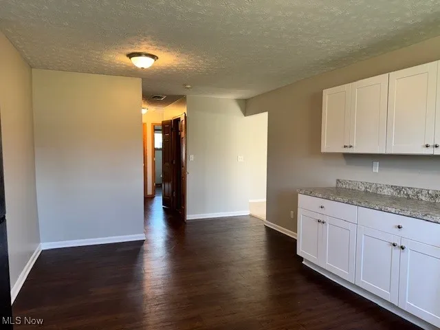 Kitchen with dark wood-style flooring, a textured ceiling, white cabinets, and light countertops