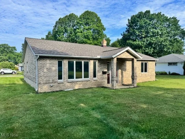 Ranch-style home featuring brick siding, a front yard, a chimney, and roof with shingles