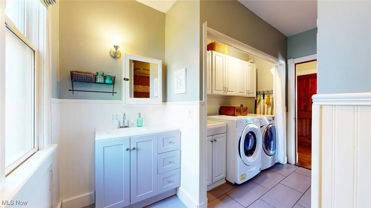 Washroom featuring independent washer and dryer, cabinet space, a wainscoted wall, and light tile patterned floors