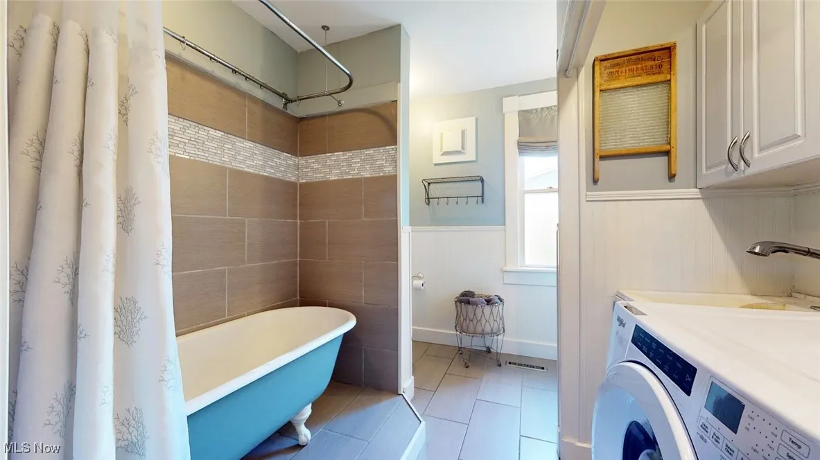 Full bathroom with washer / clothes dryer, a freestanding tub, wainscoting, and tile patterned flooring