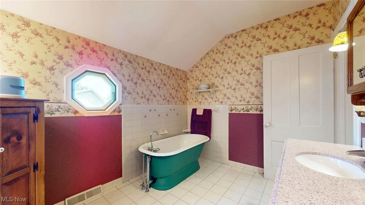 2nd Floor Full bath featuring wallpapered walls, lofted ceiling, a freestanding tub, wainscoting, and tile patterned flooring