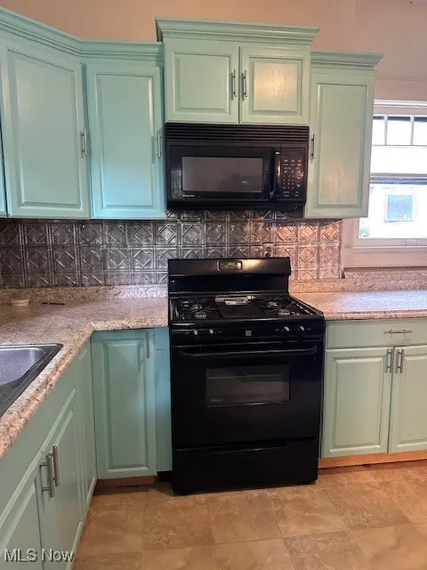 Kitchen with black range, green cabinetry, and backsplash