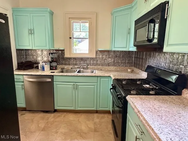 Kitchen with black appliances, tasteful backsplash, light countertops, and green cabinets