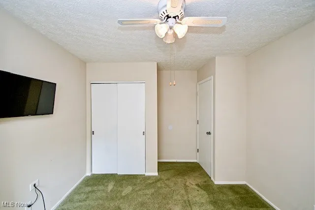 Unfurnished bedroom featuring carpet floors, a textured ceiling, a closet, and ceiling fan