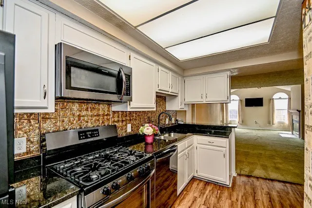 Kitchen with stainless steel appliances, white cabinetry, light wood-style flooring, open floor plan, and backsplash