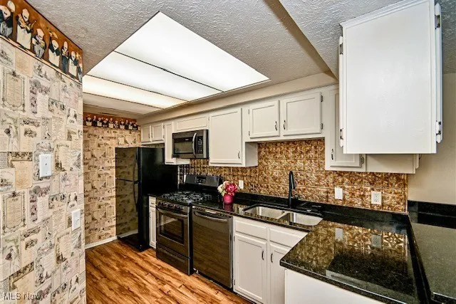 Kitchen with black appliances, white cabinets, decorative backsplash, light wood finished floors, and a textured ceiling