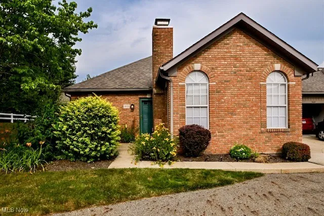 View of front of house with brick siding, a chimney, and a shingled roof